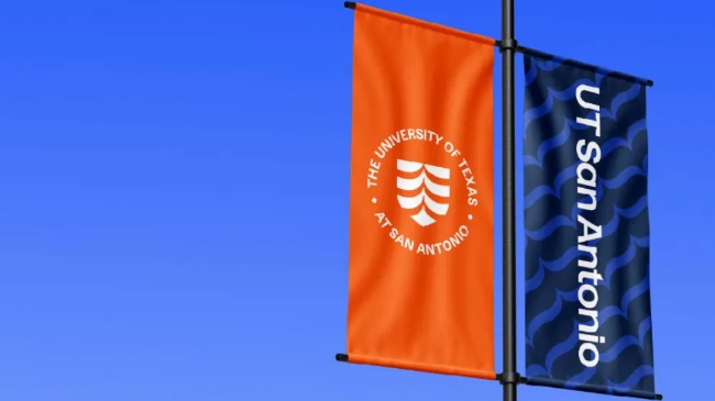Two flags on a pole, a orange and blue, with the University of Texas at San Antonio logo on them